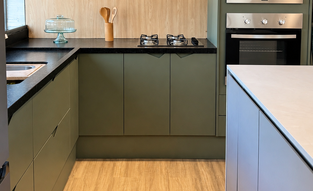 Cozinha planejada verde oliva com detalhes em madeira, bancada escura e iluminação em LED no showroom do Studio V